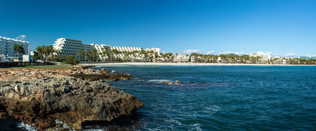A coastal resort with a rocky shoreline, palm trees, and beachfront hotels.