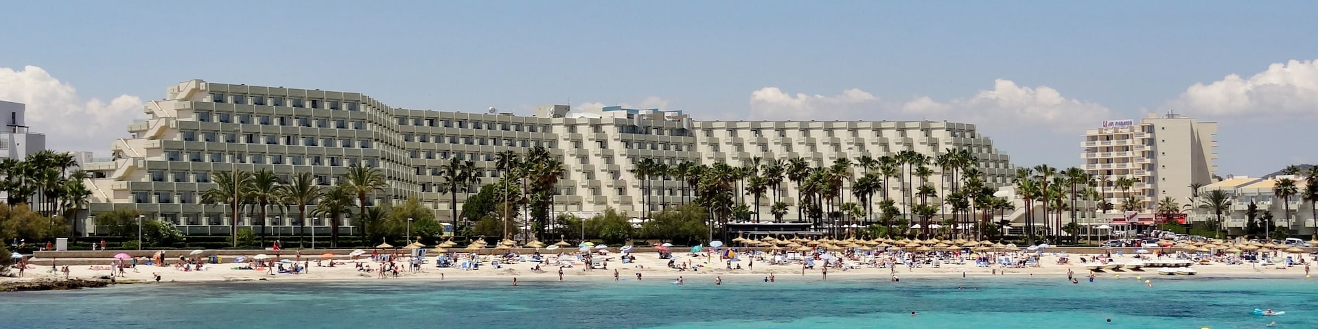Un hotel frente a la playa con piscina y sombrillas.