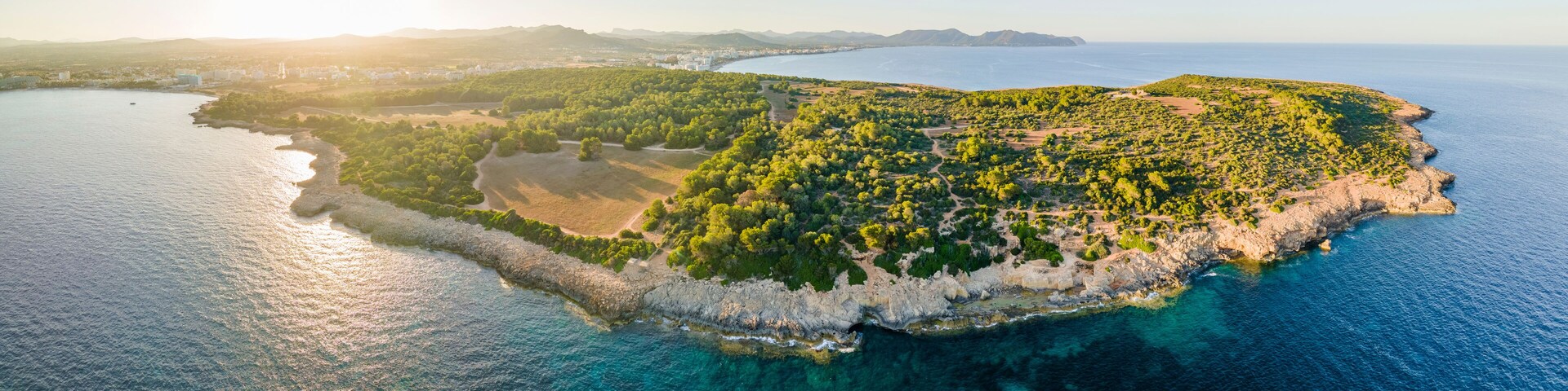 Vista aérea de una isla costera con abundante vegetación, costas rocosas y aguas azules cristalinas.