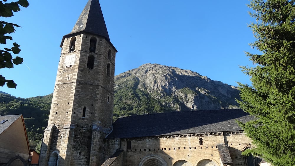 A historic stone church with a tall bell tower and a mountain in the background.