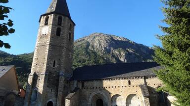 A historic stone church with a tall bell tower and a mountain in the background.