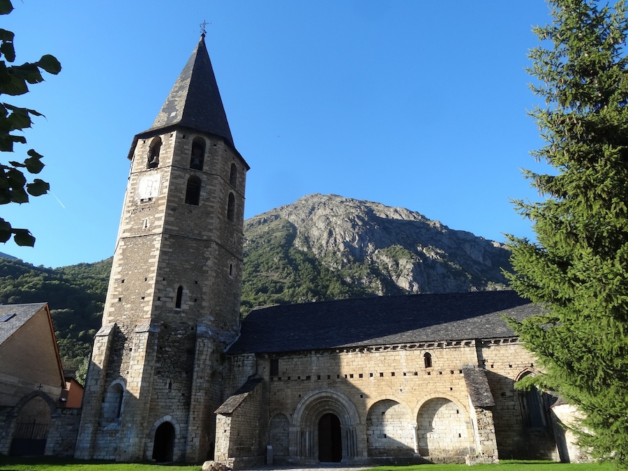 A historic stone church with a tall bell tower and a mountain in the background.