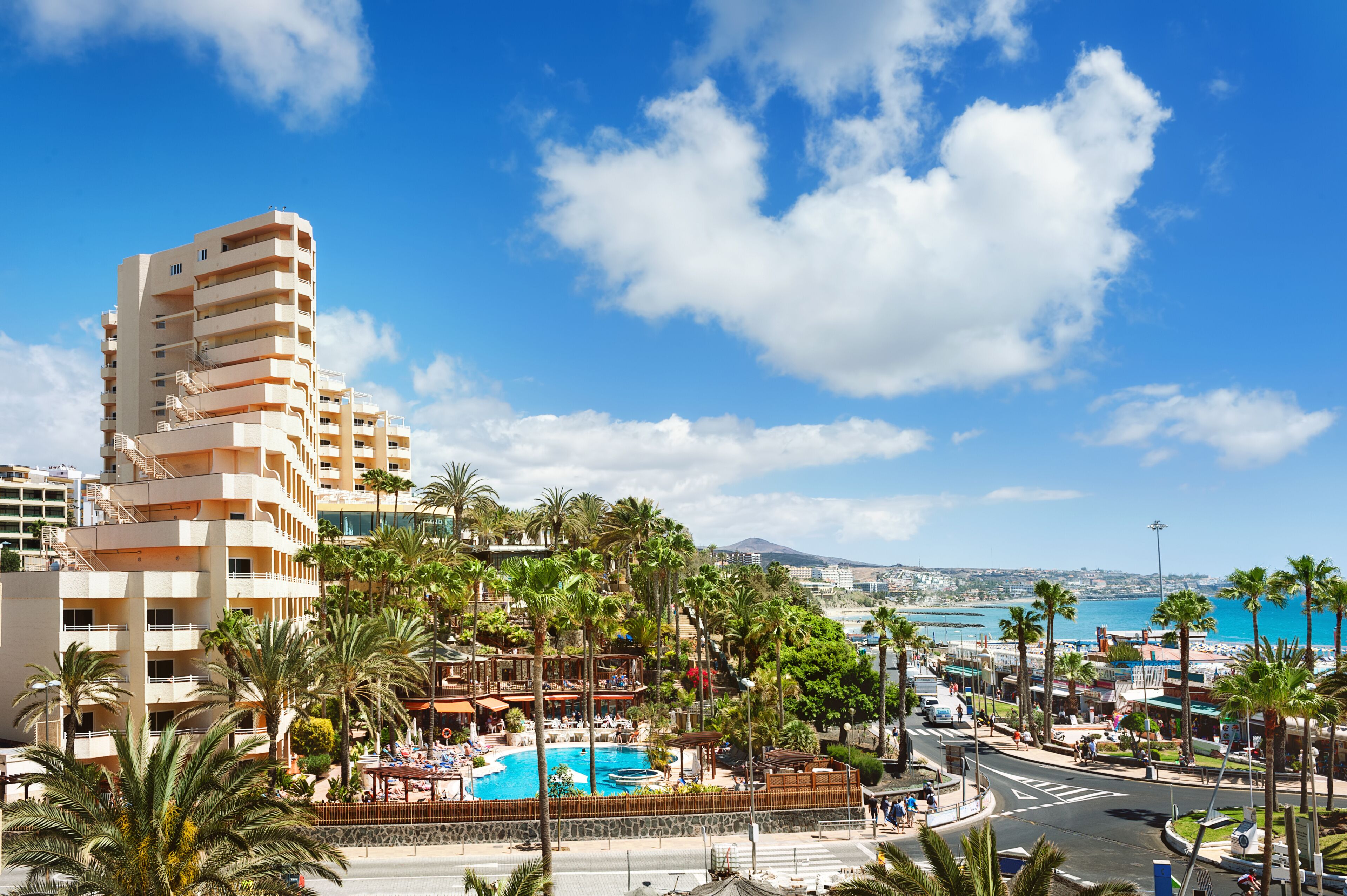 A resort with a swimming pool, palm trees, and a view of the sea.