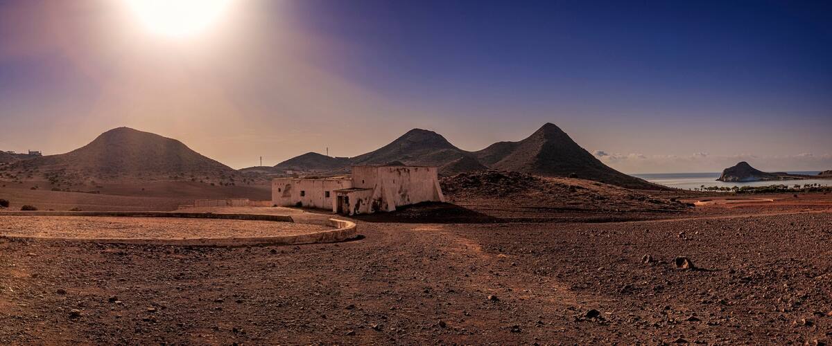 A desert landscape with a circular road, a small building, and mountains in the background.