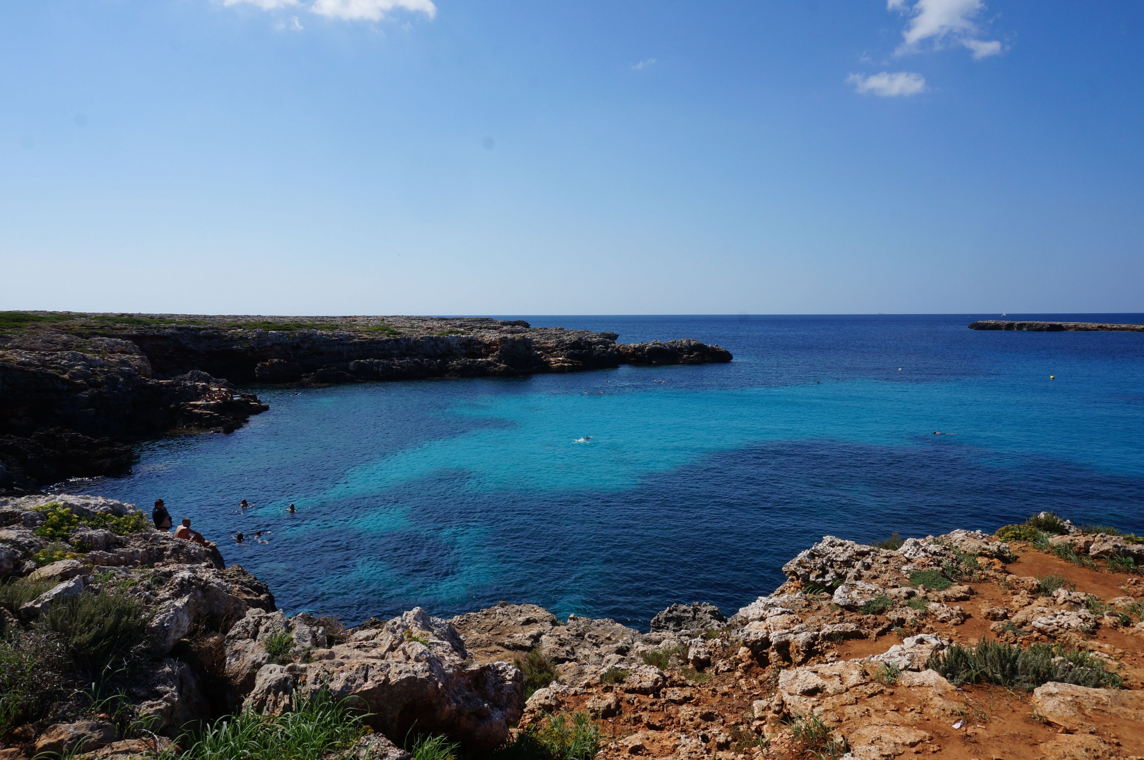 A coastal landscape with rocky cliffs, clear blue sea, and a distant island.