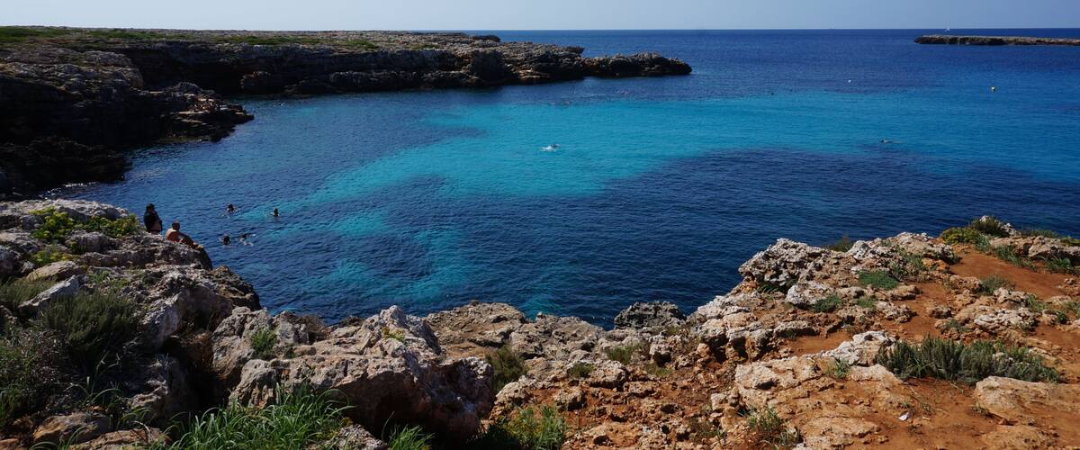 A coastal landscape with rocky cliffs, clear blue sea, and a distant island.