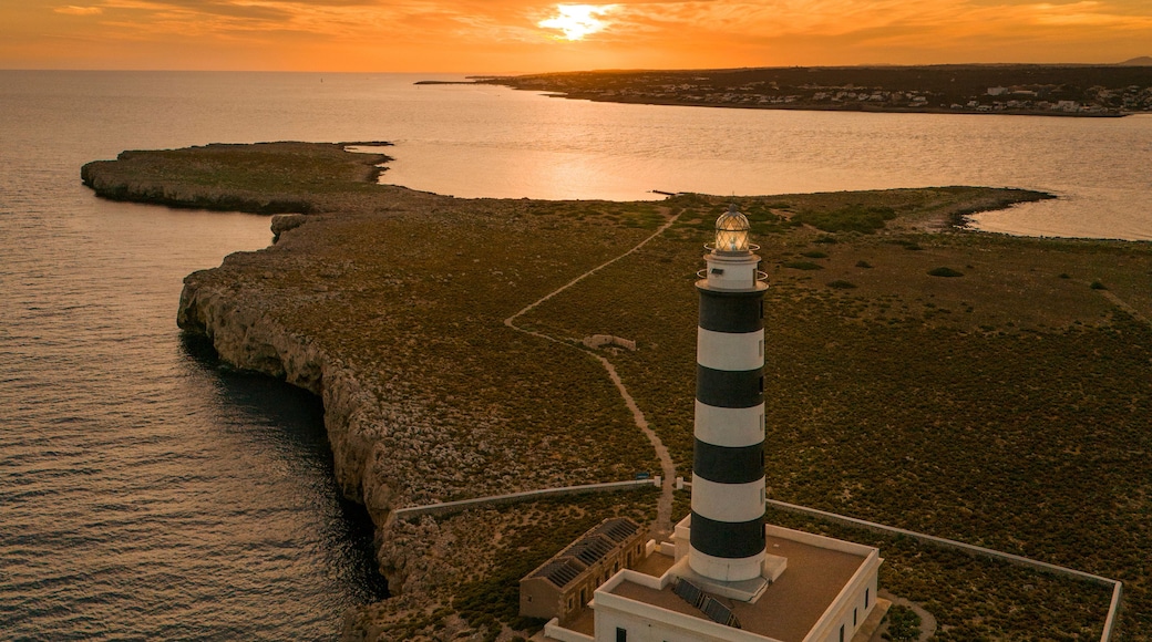 Aerial view of Cap de l'Isla de l'Aire lighthouse at sunset with tranquil sea and rocky coastline, Punta Prima, Menorca, Balearic Islands, Spain.