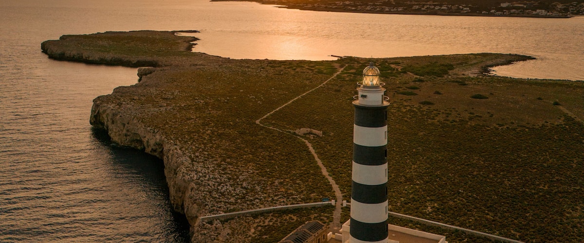 A coastal landscape with a lighthouse, rocky terrain, and a sunset over the sea.