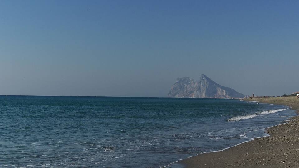 A beach with a rocky shoreline and a prominent mountain in the background.