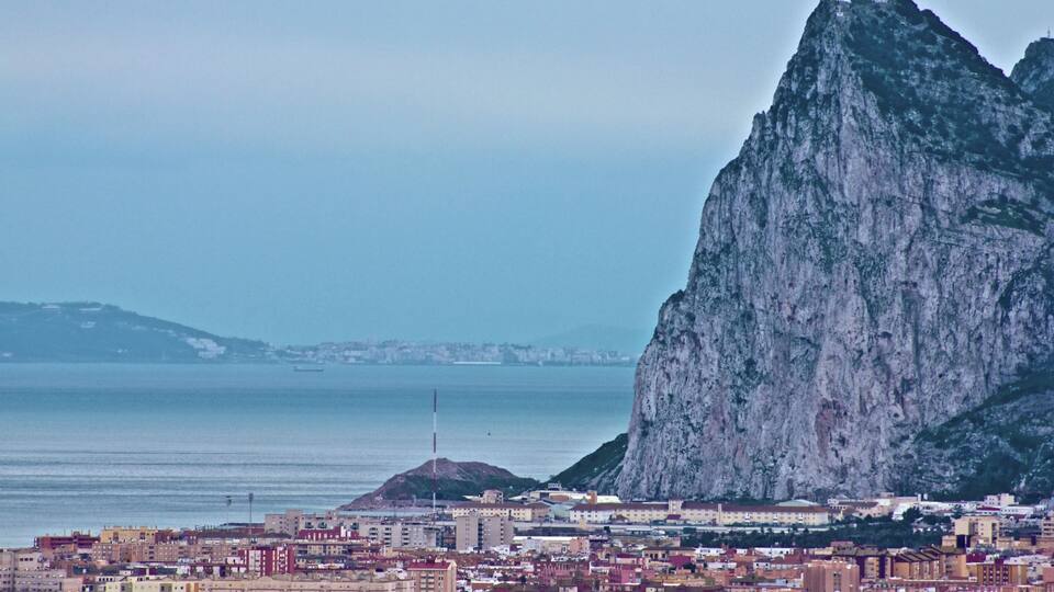 A coastal cityscape with a prominent mountain and a body of water.