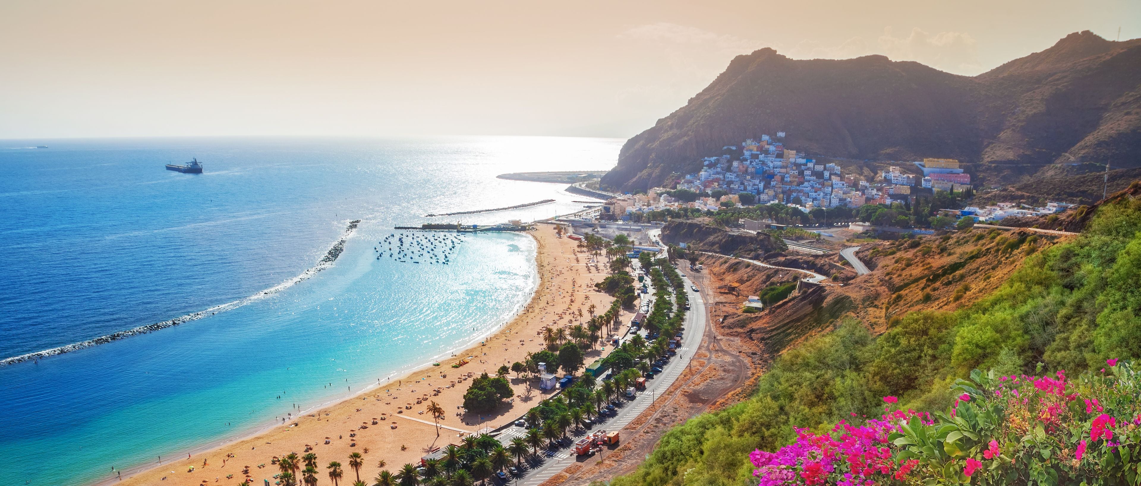 A coastal town with a beach, a pier, and a mountainous backdrop.