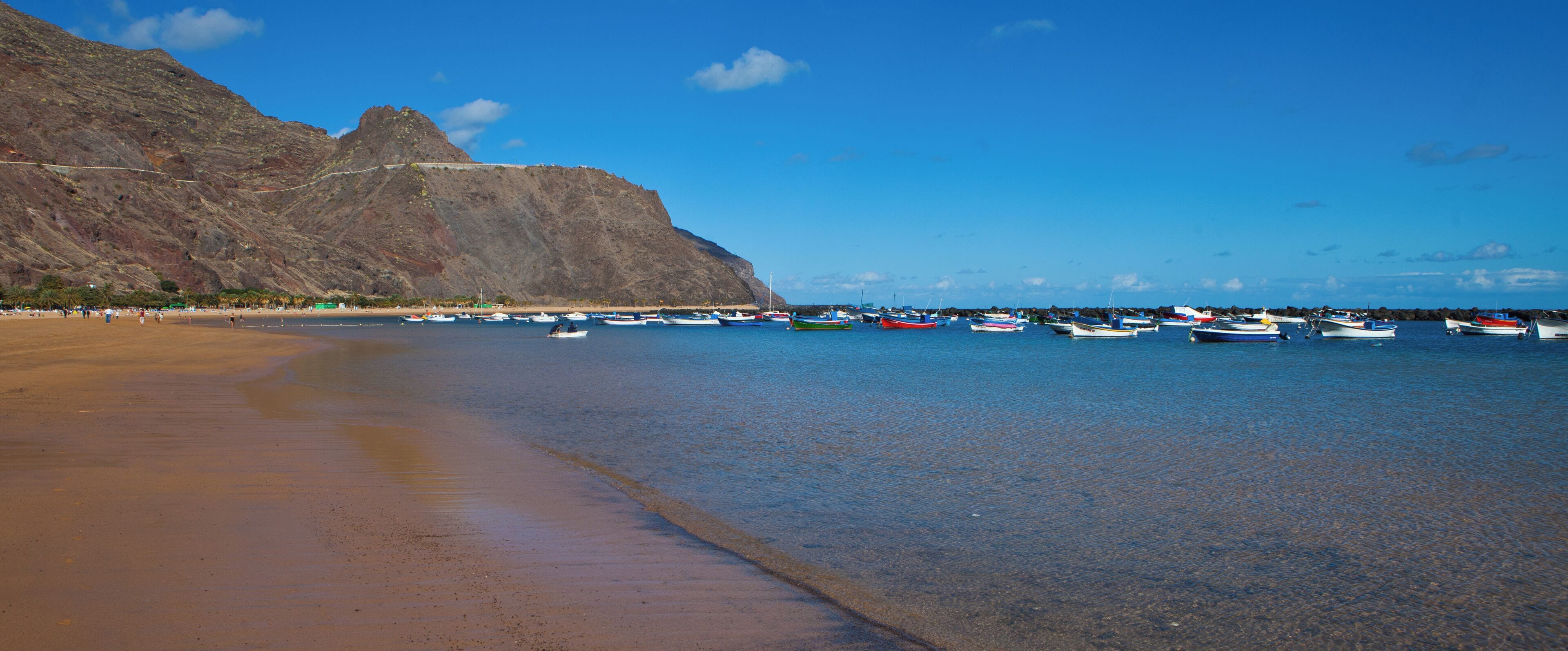 A beach with boats, a mountain, and clear blue sky.