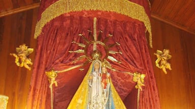 A religious statue with a red and gold canopy, surrounded by flowers and candles.