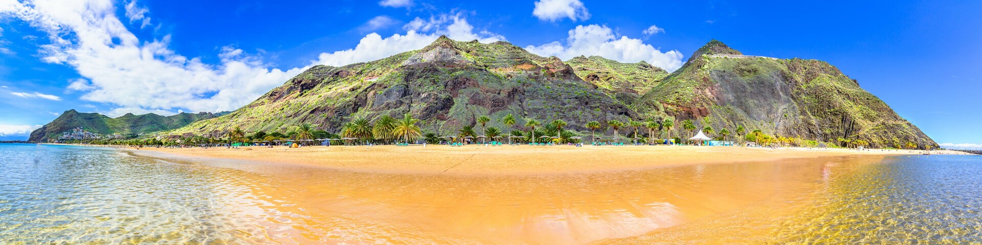 Uma praia com águas turquesa cristalinas, uma costa arenosa e um conjunto de montanhas ao fundo.