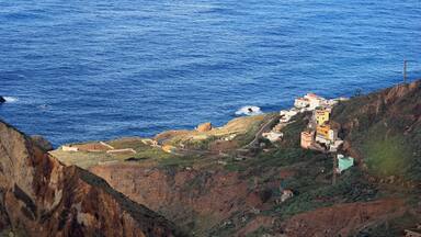 A coastal landscape with a cliff overlooking the sea, featuring colorful buildings and a winding road.