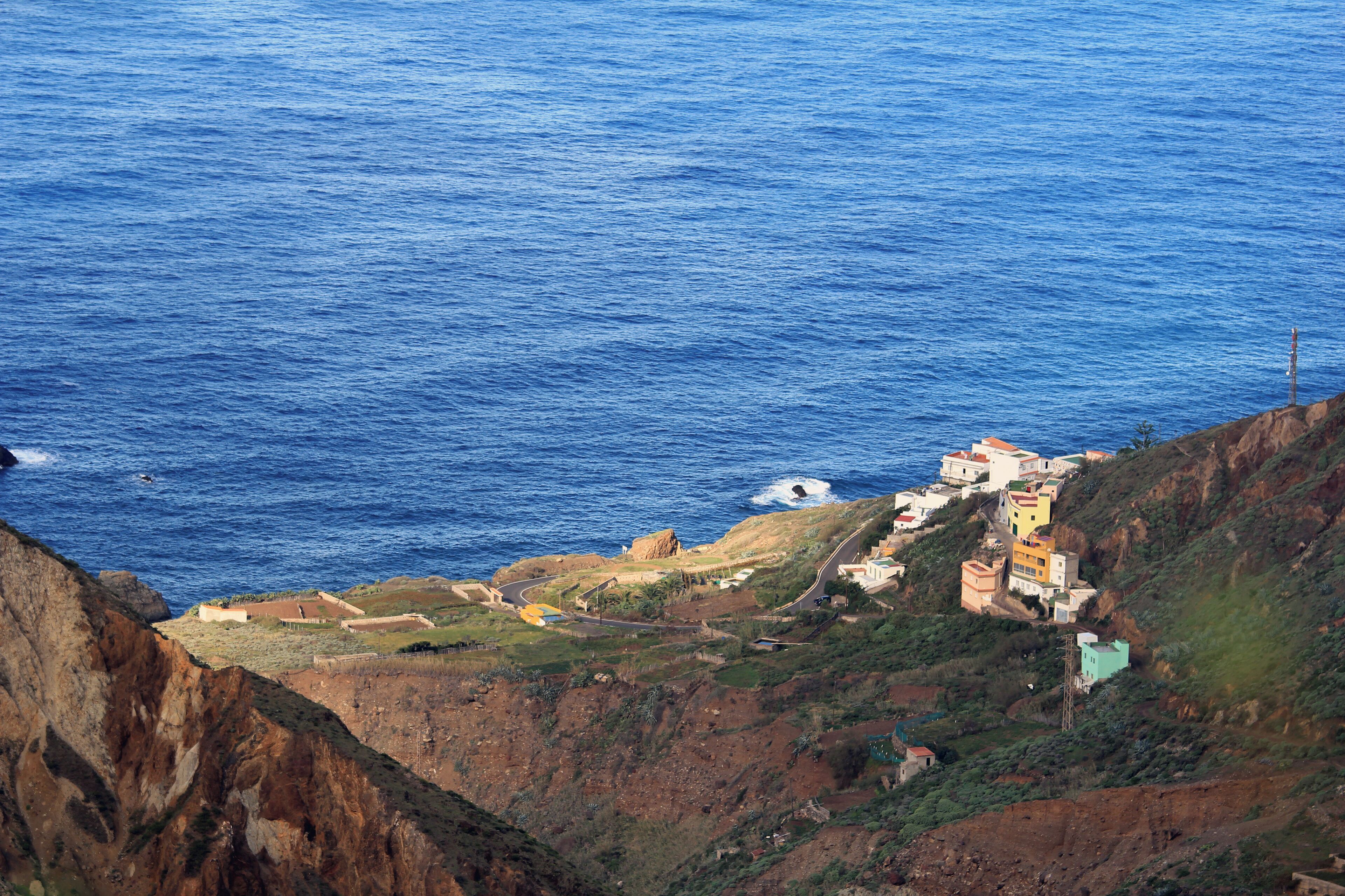 A coastal landscape with a cliff overlooking the sea, featuring colorful buildings and a winding road.