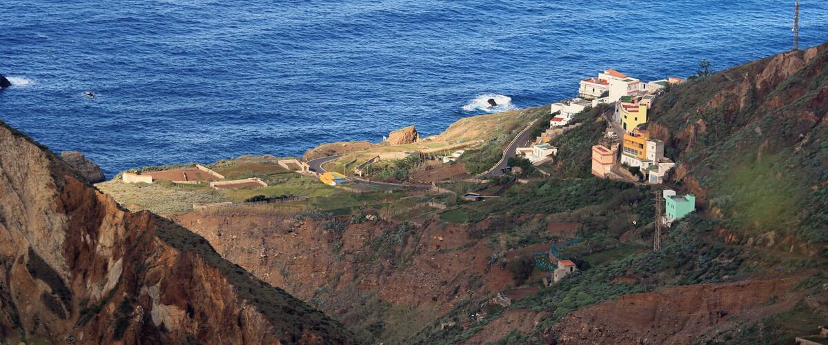 A coastal landscape with a cliff overlooking the sea, featuring colorful buildings and a winding road.