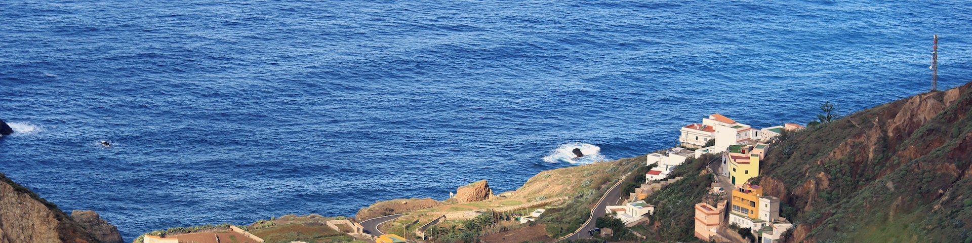 A coastal landscape with a cliff overlooking the sea, featuring colorful buildings and a winding road.