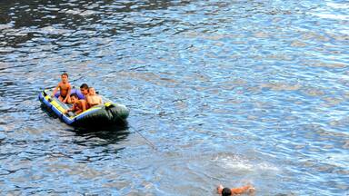 A stone pier extending into a body of water with people on a raft and a swimmer.