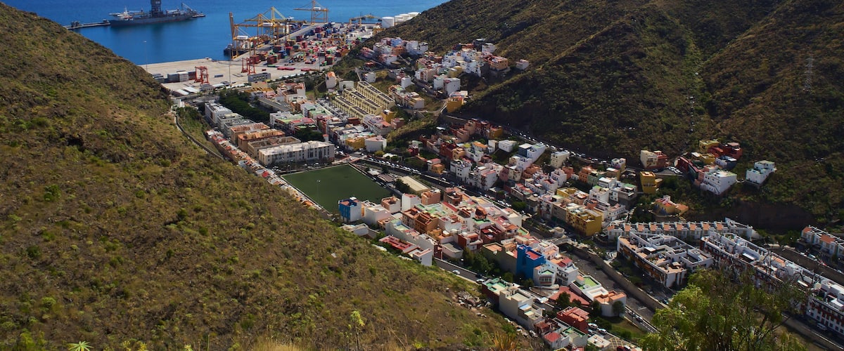 A coastal town with a port, hills, and a clear blue sky.