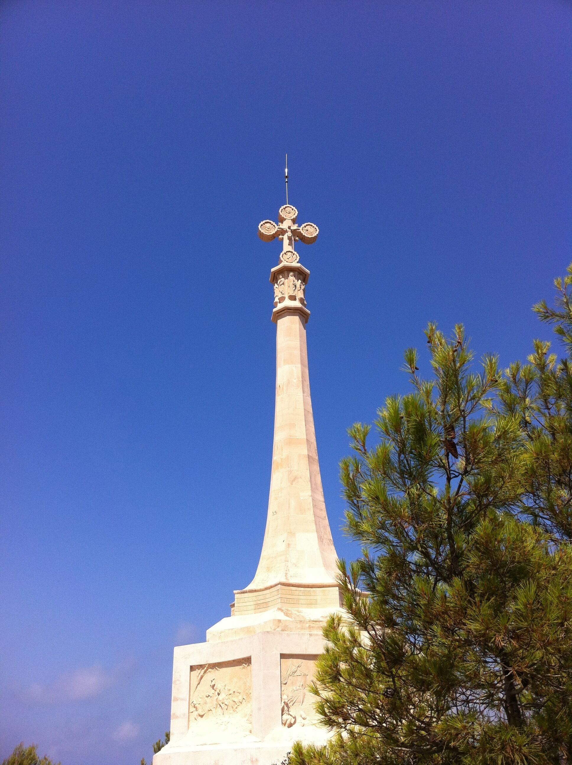 Un alto monumento sormontato da una croce, circondato da alberi.
