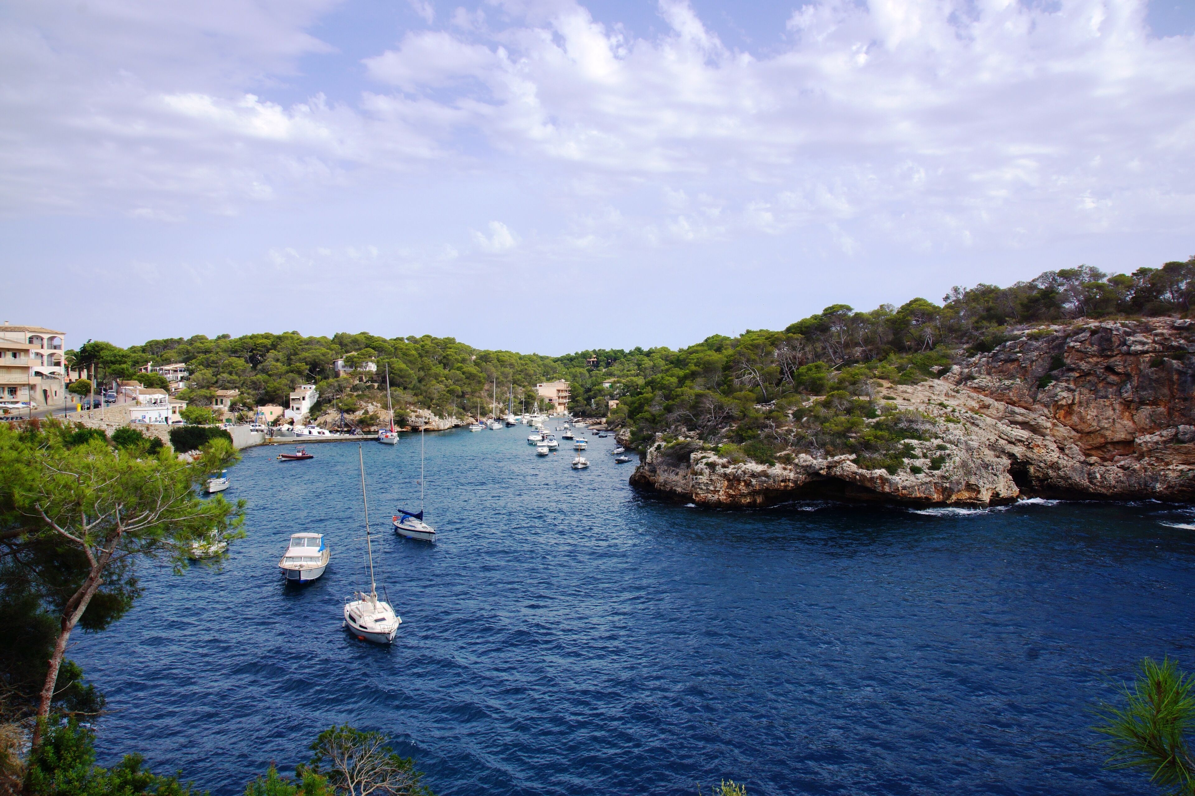 A coastal town with boats anchored in the water, rocky cliffs, and buildings on the hillside.