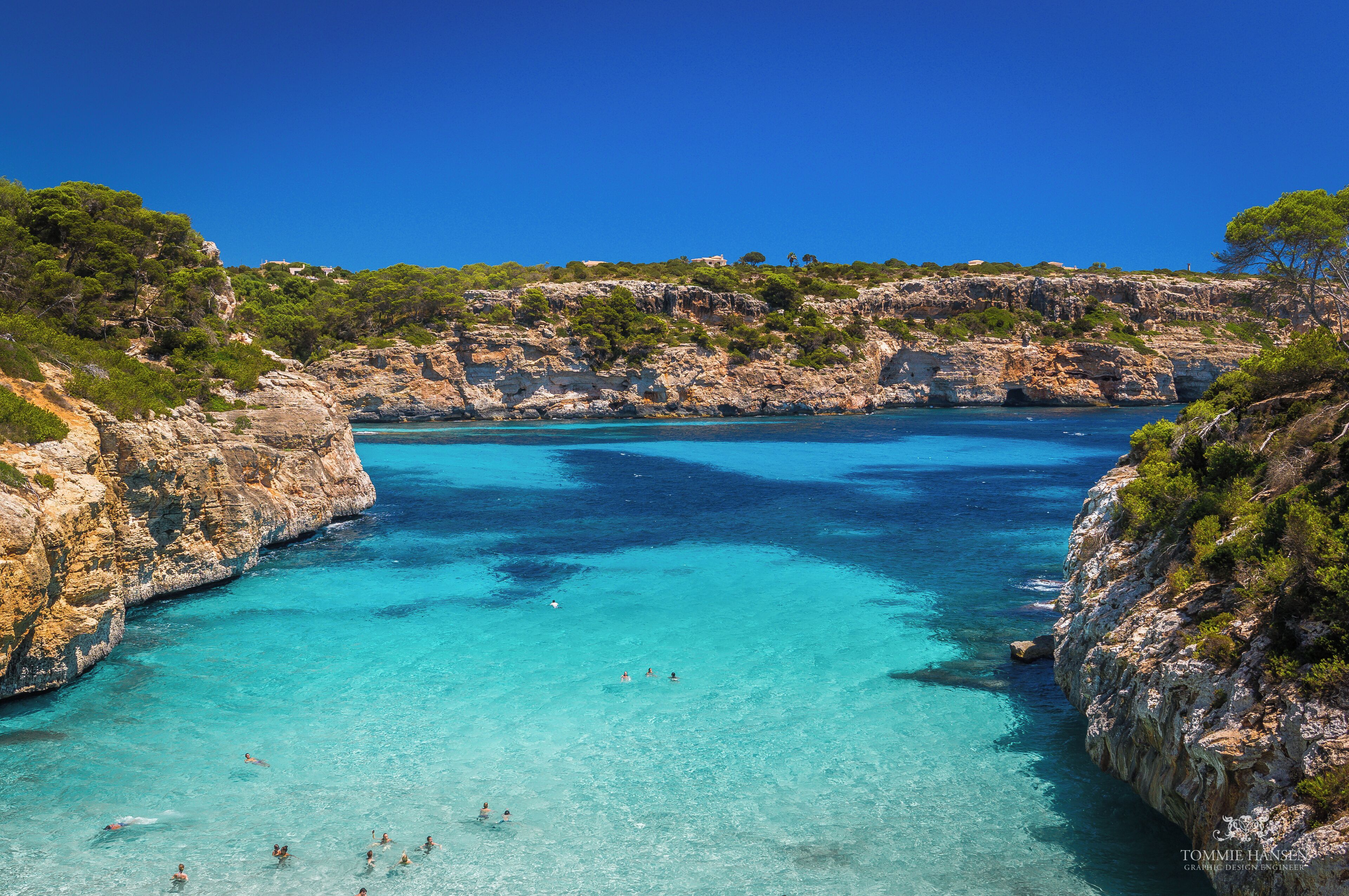 A coastal landscape with clear turquoise waters, rocky cliffs, and sparse vegetation.