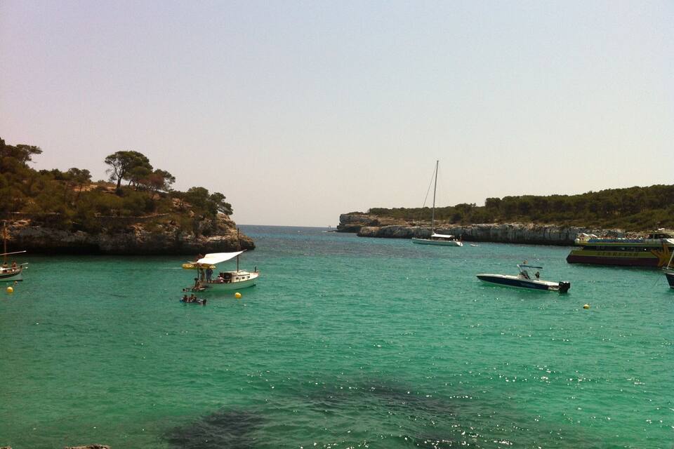 A coastal scene with clear turquoise waters, boats, and rocky cliffs.