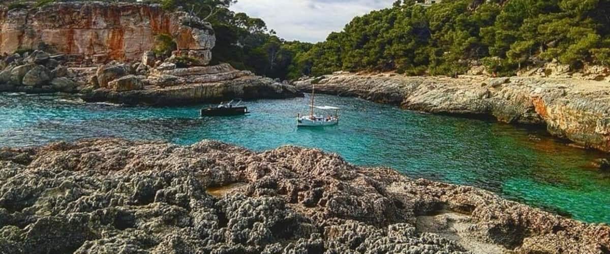 A coastal landscape with rocky cliffs, clear turquoise waters, and a small boat anchored near the shore.