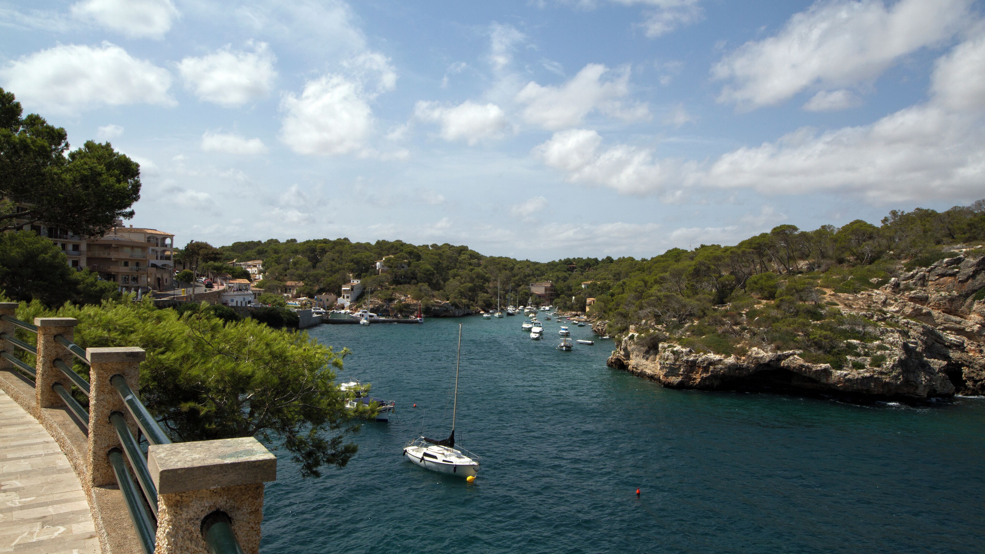 A coastal town with boats docked along the shore, surrounded by rocky cliffs and lush greenery.