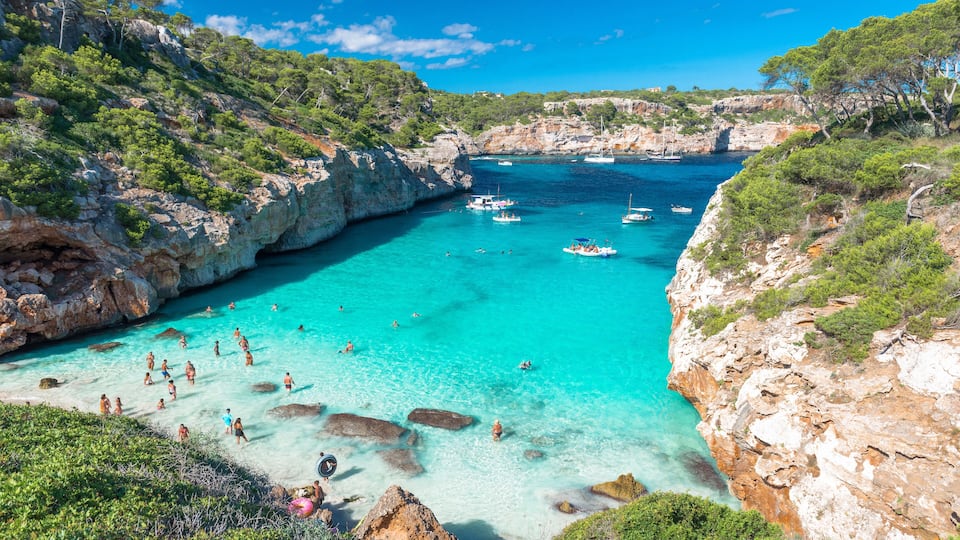 A coastal bay with clear turquoise waters, rocky cliffs, and boats anchored near the shore.