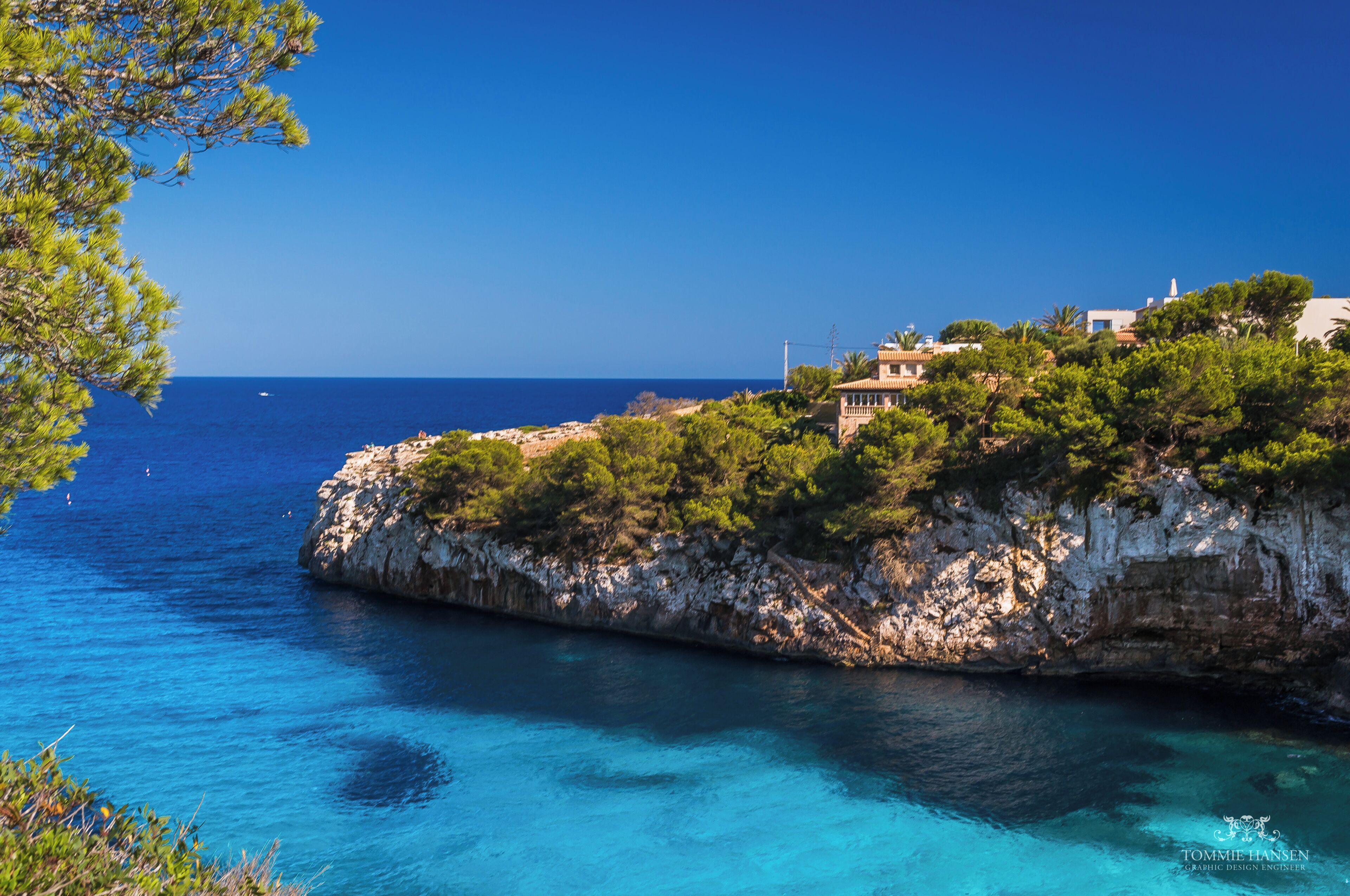 A coastal landscape with clear blue waters, rocky cliffs, and buildings on top.