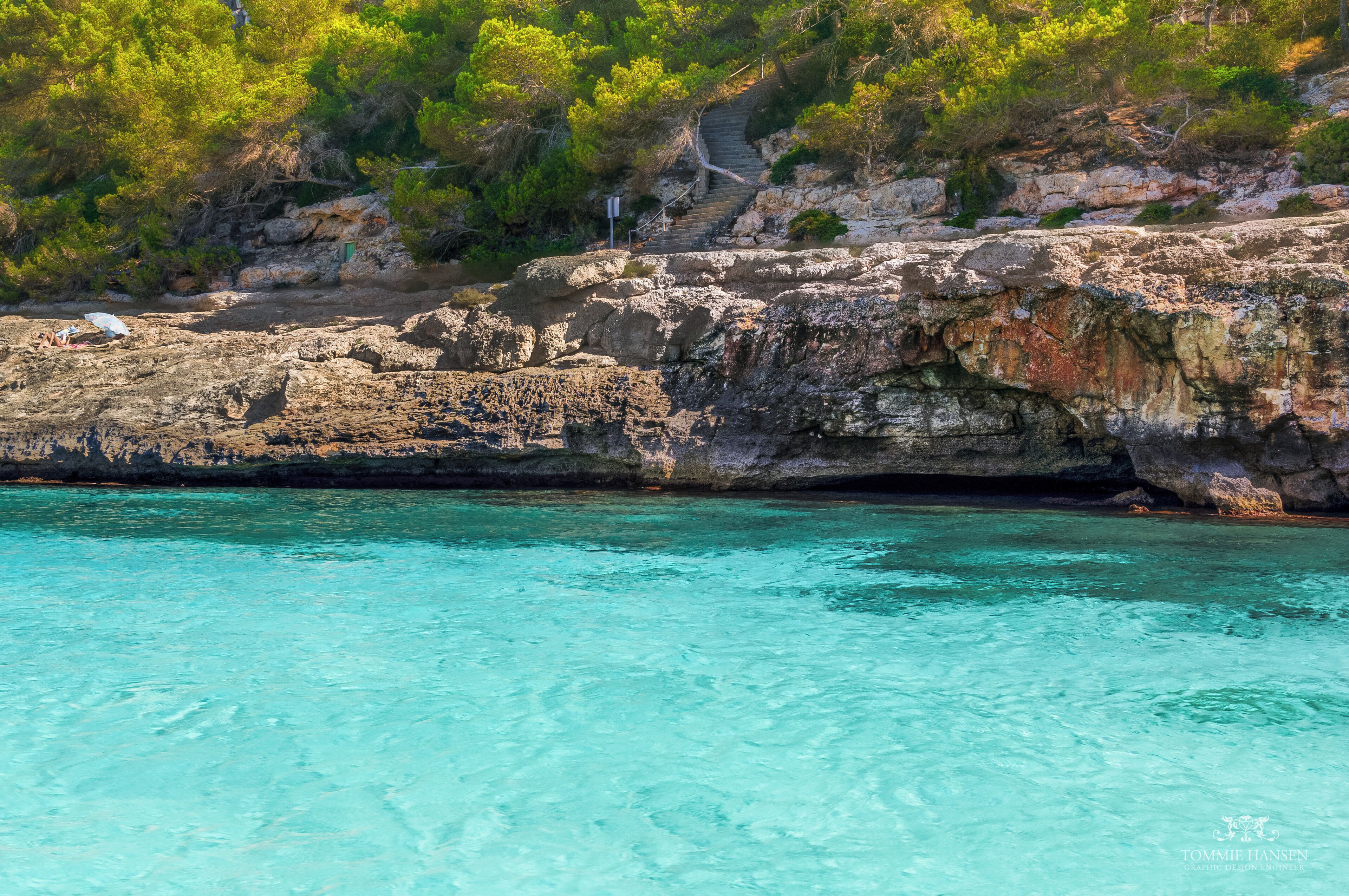A rocky coastline with clear turquoise water and green vegetation.