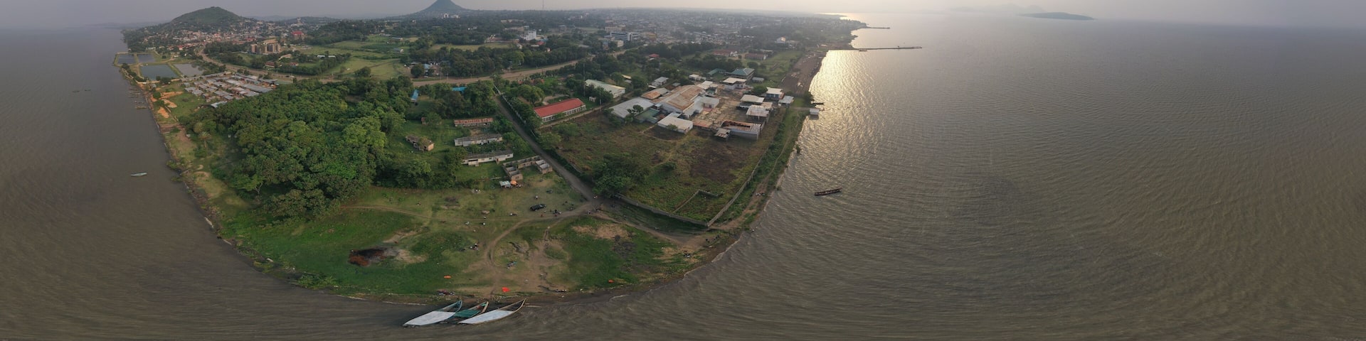 Aerial view of boats resting on the shores of Lake Victoria, the city sprawling with buildings and lush greenery under a hazy sky, Kisumu, Homa Bay, Kenya.