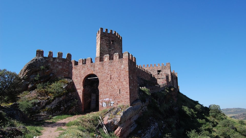 A historic stone castle with a central tower and battlements, surrounded by rocky terrain and greenery.