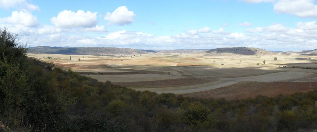 A vast landscape with rolling hills, fields, and a small cluster of buildings.