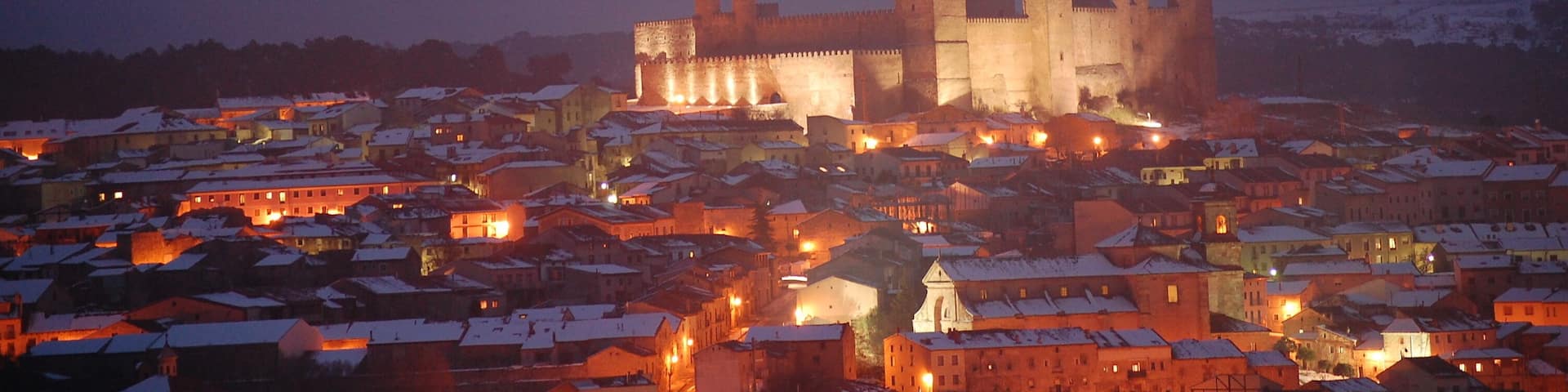 A medieval castle surrounded by a snow-covered town at dusk.