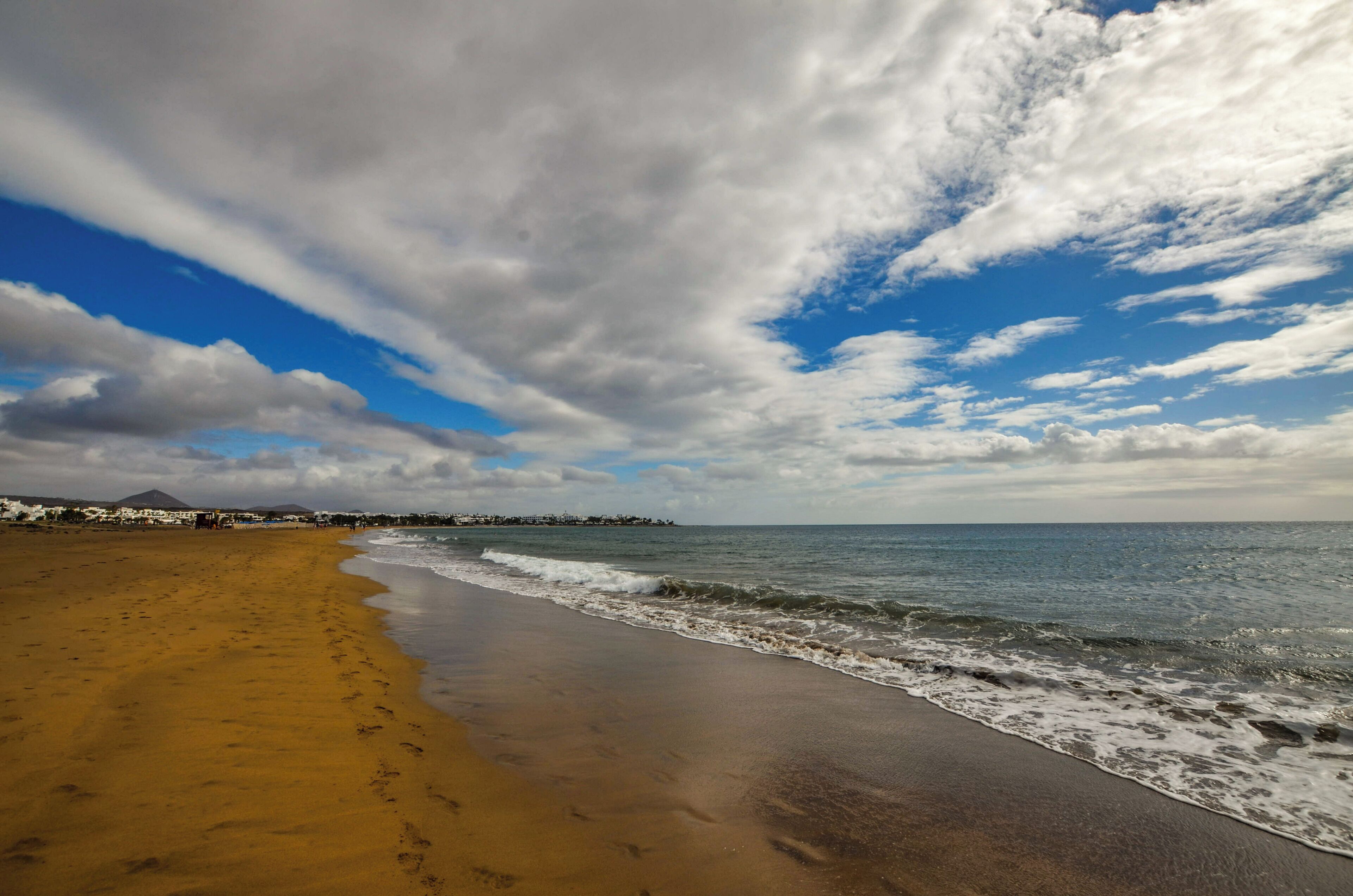 A beach with a sandy shore, ocean waves, and a cloudy sky.