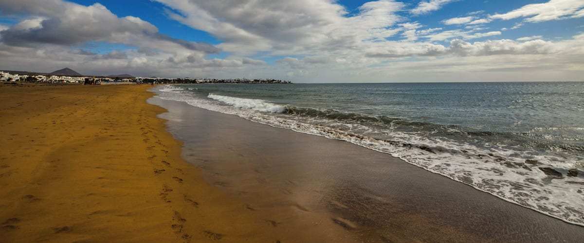A beach with a sandy shore, ocean waves, and a cloudy sky.