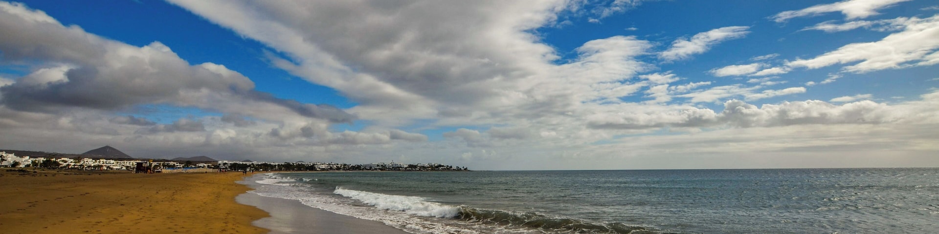 A beach with a sandy shore, ocean waves, and a cloudy sky.