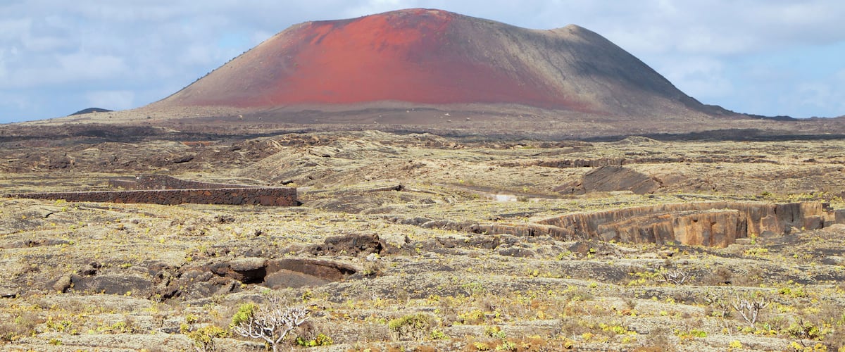 A volcanic landscape with a prominent red mountain and rocky terrain.