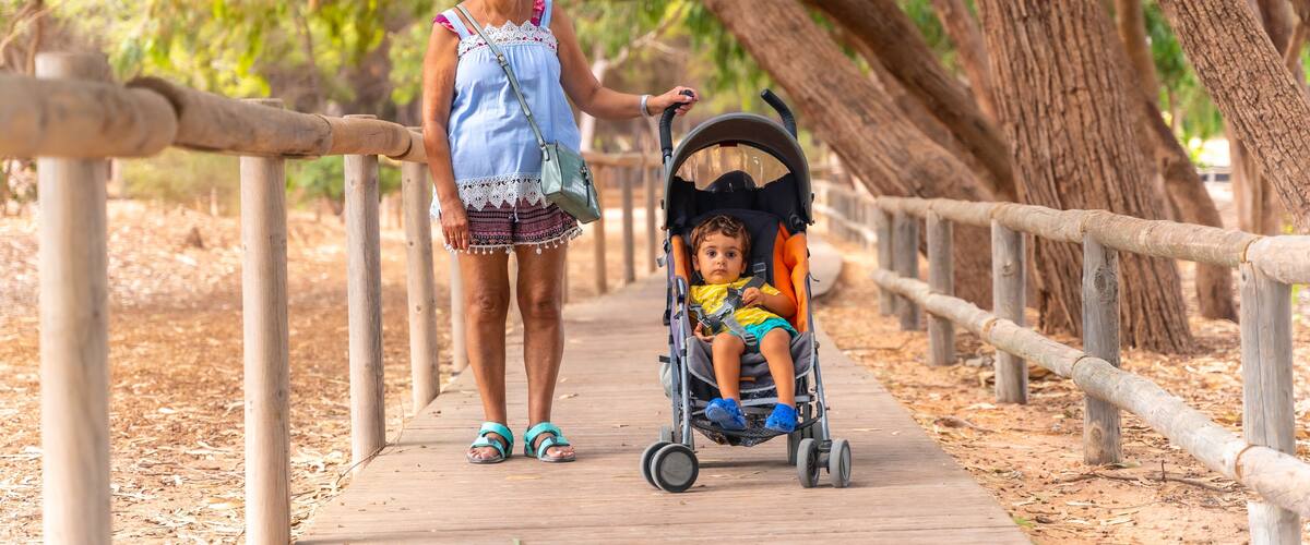A woman walking with a stroller on a wooden boardwalk surrounded by trees.