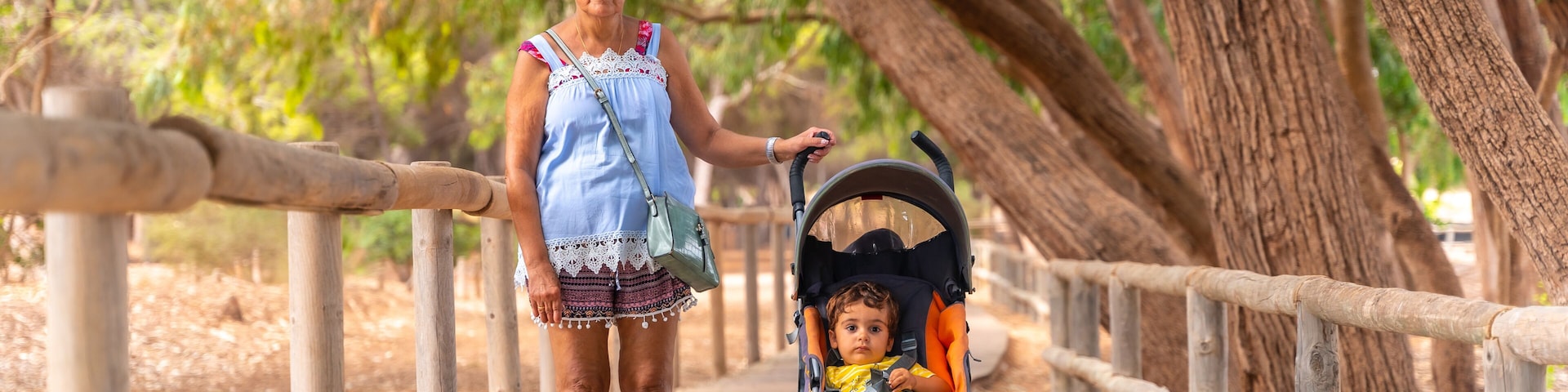 A woman walking with a stroller on a wooden boardwalk surrounded by trees.