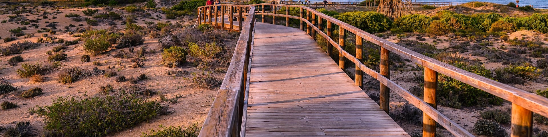 A wooden boardwalk leading to a beach with a sunset in the background.