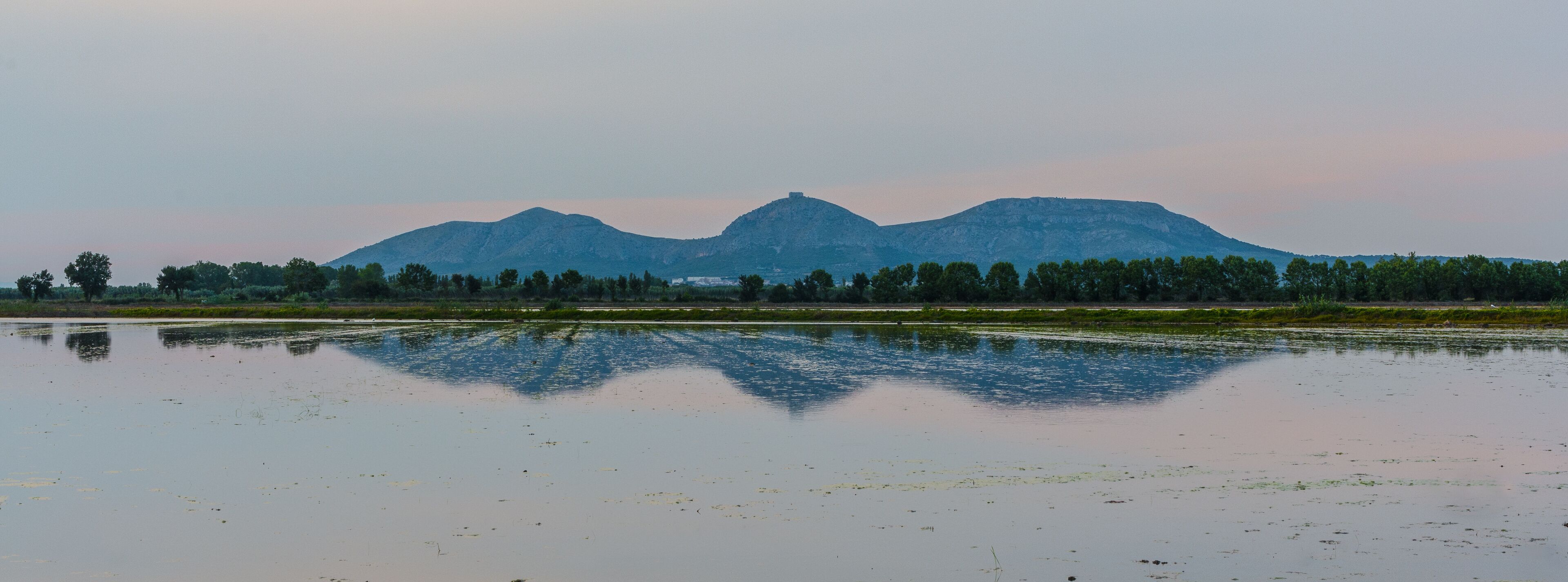 A calm lake with reflections of trees and mountains in the background.