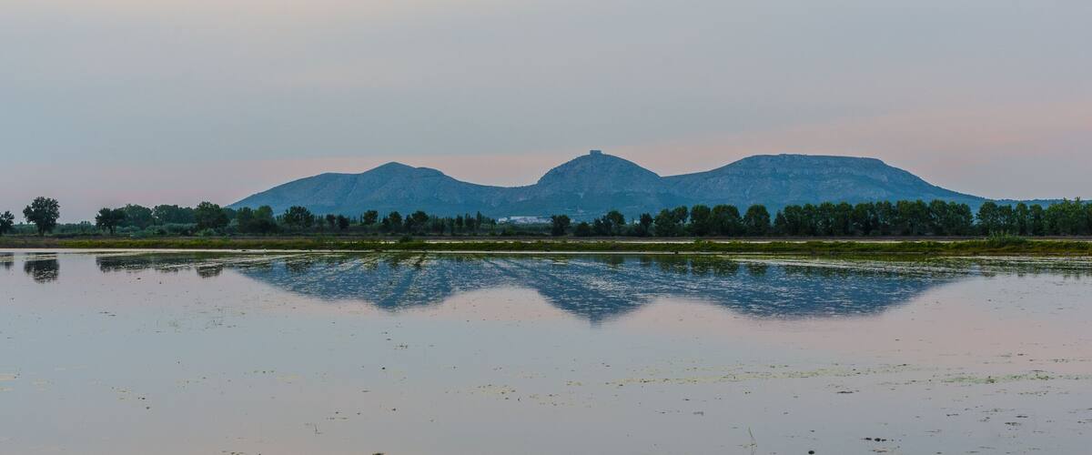 A calm lake with reflections of trees and mountains in the background.