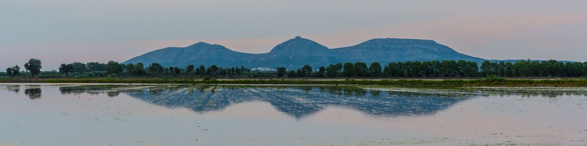 A calm lake with reflections of trees and mountains in the background.