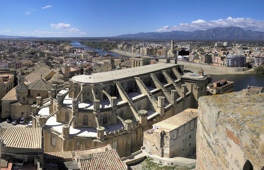 Un paisaje urbano histórico con una catedral destacada, un río y montañas al fondo.