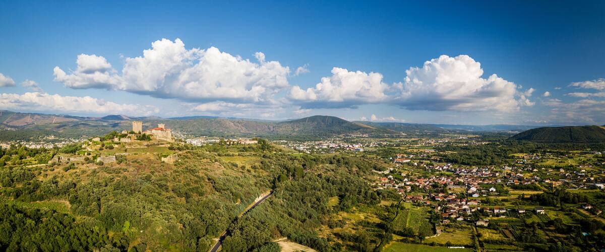 A castle on a hill overlooking a town surrounded by mountains and greenery.