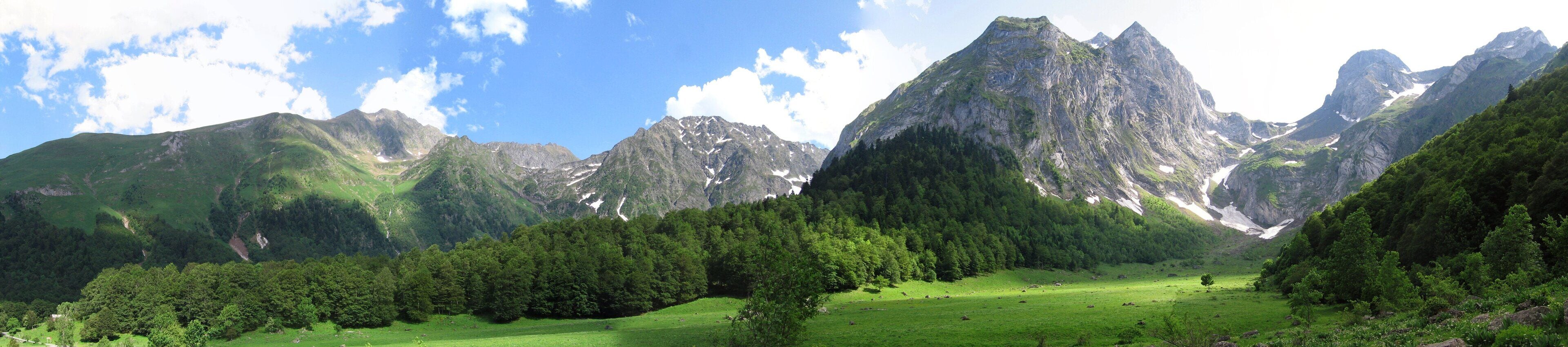 A mountainous landscape with a valley, dense forest, and a clear sky.